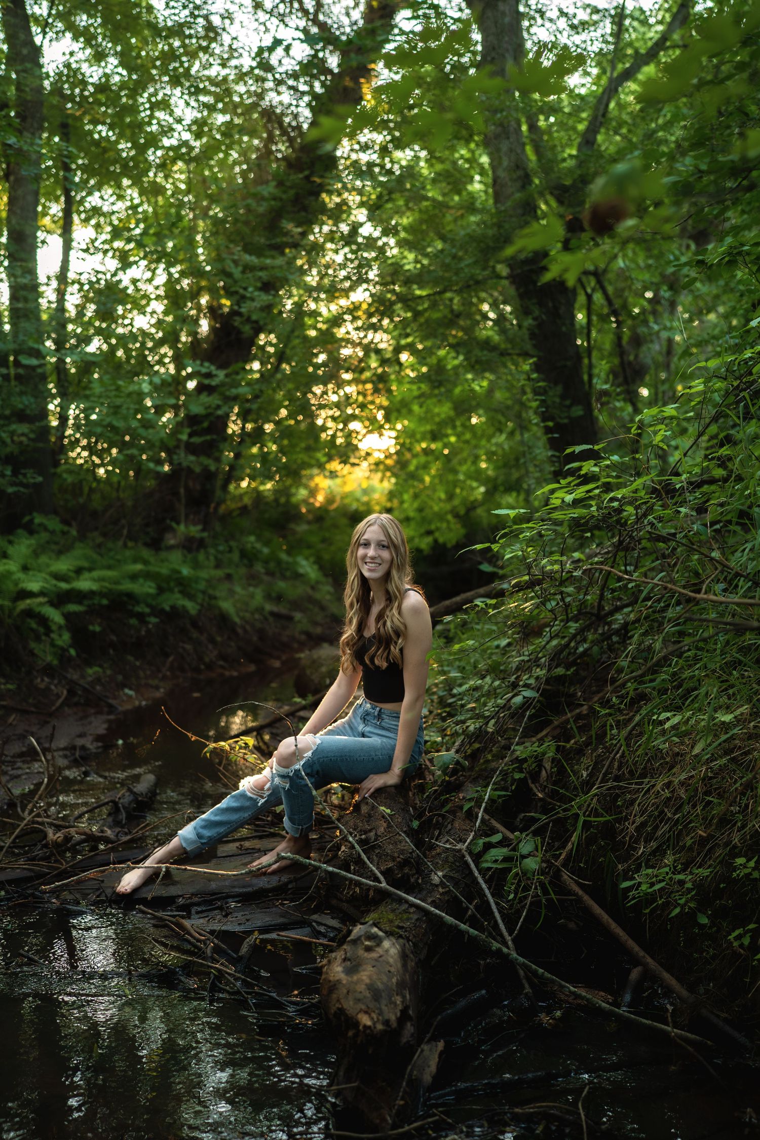 Scenic outdoor portrait by a stream with fallen logs and natural woodland backdrop.