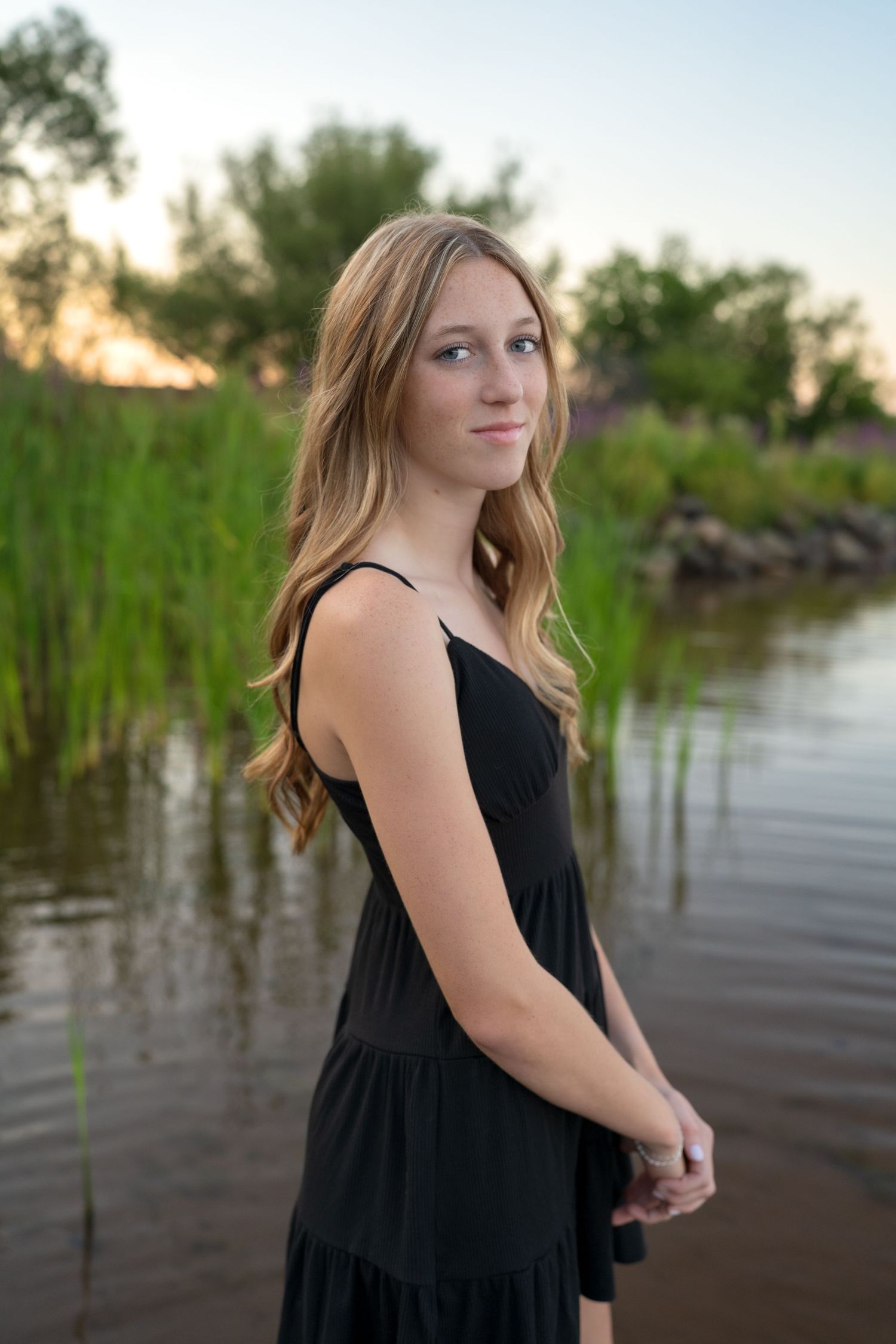 A serene outdoor portrait session near a lake with tall reeds and cattails at sunset.