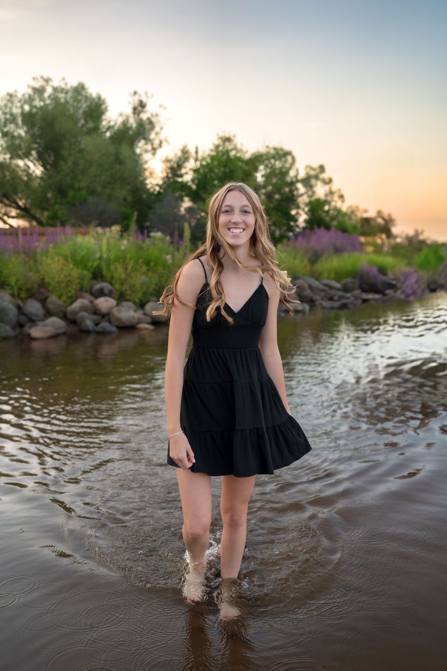 A person in a black summer dress splashes and plays in the shallow waters of a lake during golden hour.