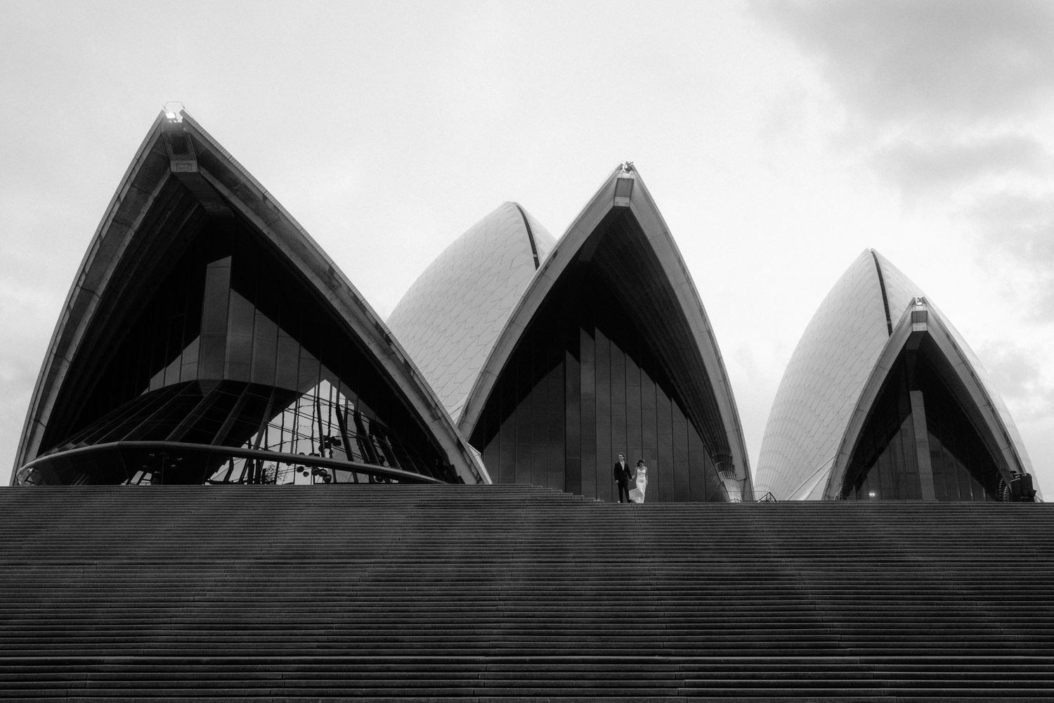Black and white architectural photograph showing the iconic Sydney Opera House sails against a cloudy sky.