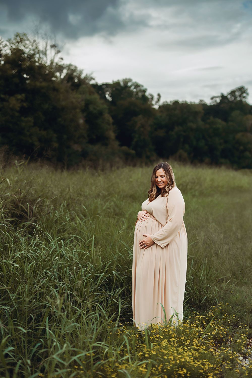 Mom in flowing beige dress in a wildflower field under moody clouds.