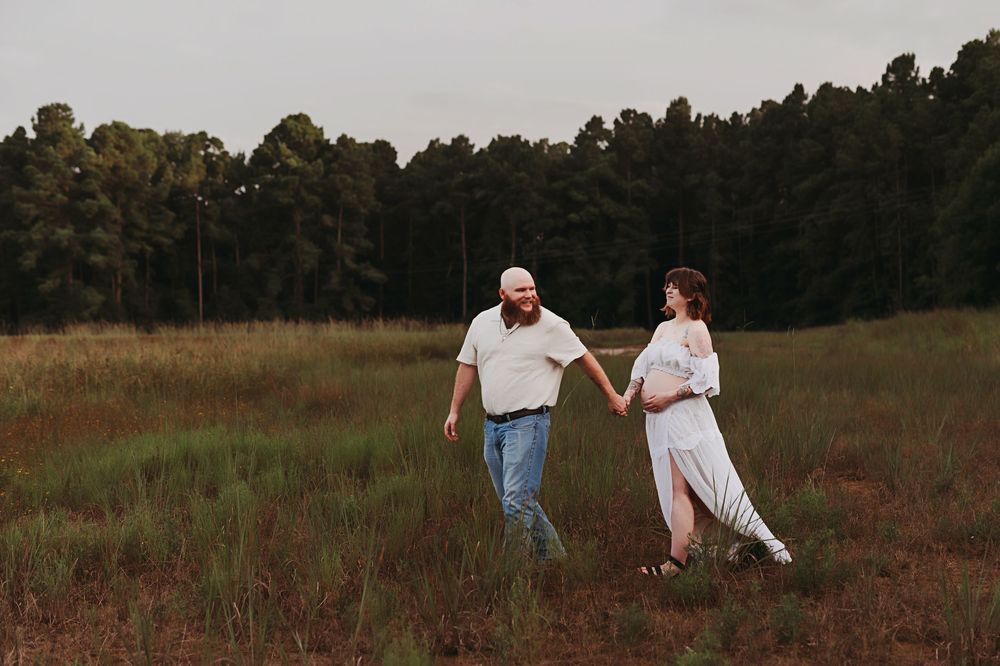 A couple walks together through a rustic autumn field at sunset while holding hands.