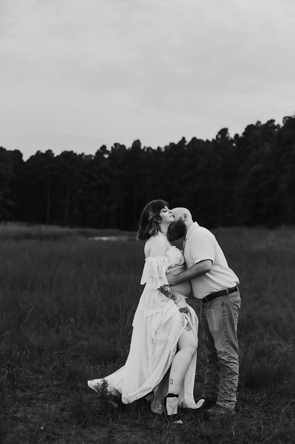 A romantic black and white photo series showing a couple embracing in a grassy field at dusk.