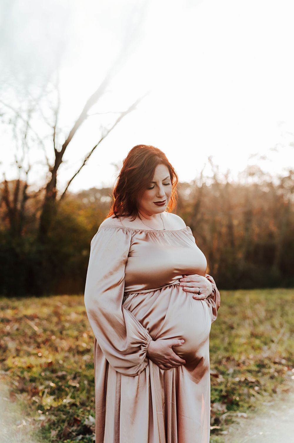 A mother in a beige dress embraces her baby in a tender outdoor photoshoot during golden hour.
