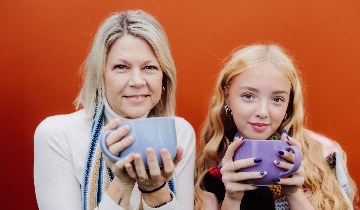 Two people share laughter while drinking hot beverages from blue mugs at a cafe.