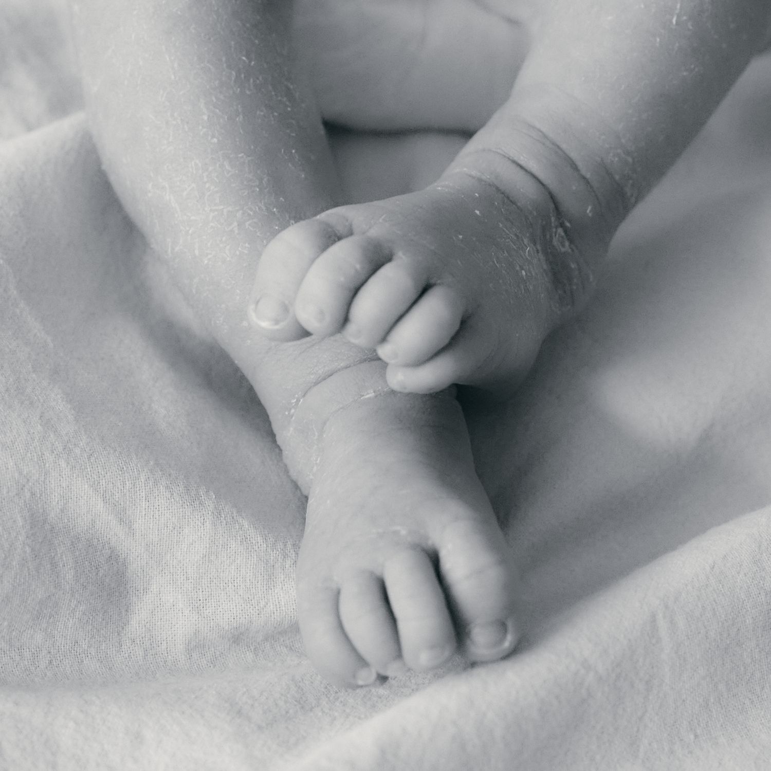 Close-up black and white image of baby's tiny feet on soft textured background.