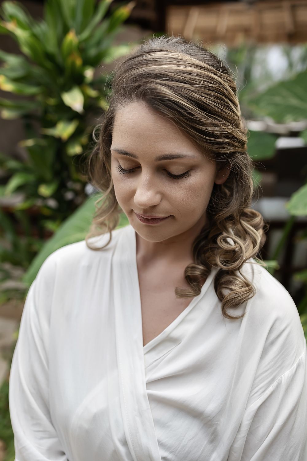 Elegant bridal portrait showing soft curled hairstyle against tropical garden background.
