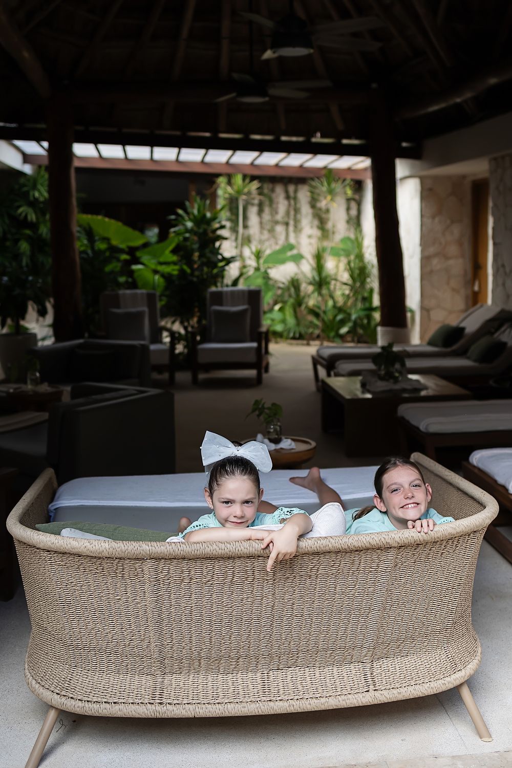 Three connected photos show children playfully peeking over the back of a large beige upholstered couch in a modern space.