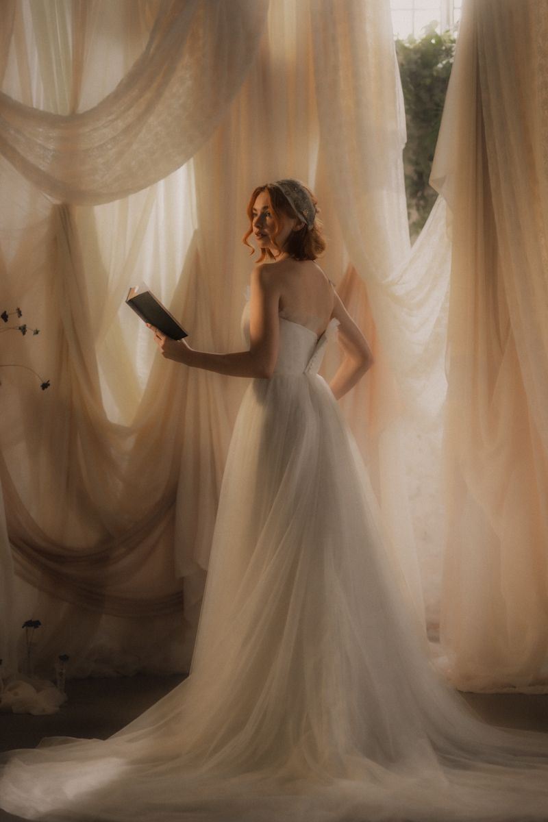 A dreamy bridal portrait with flowing white gown and sheer curtains creating an ethereal atmosphere in soft lighting.