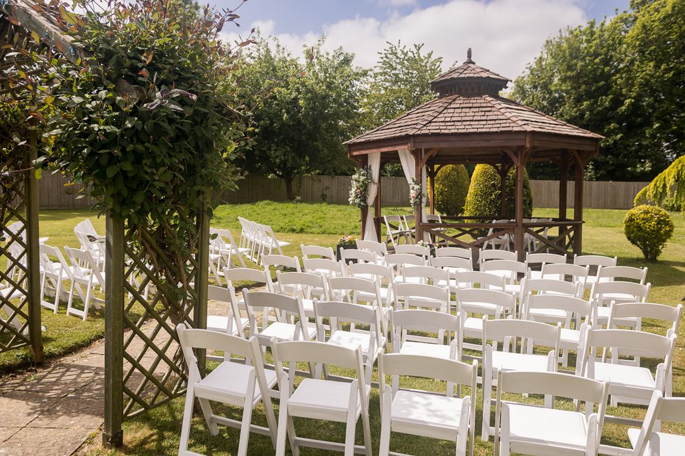 Outdoor wedding ceremony setup with white chairs and gazebo surrounded by lush greenery.