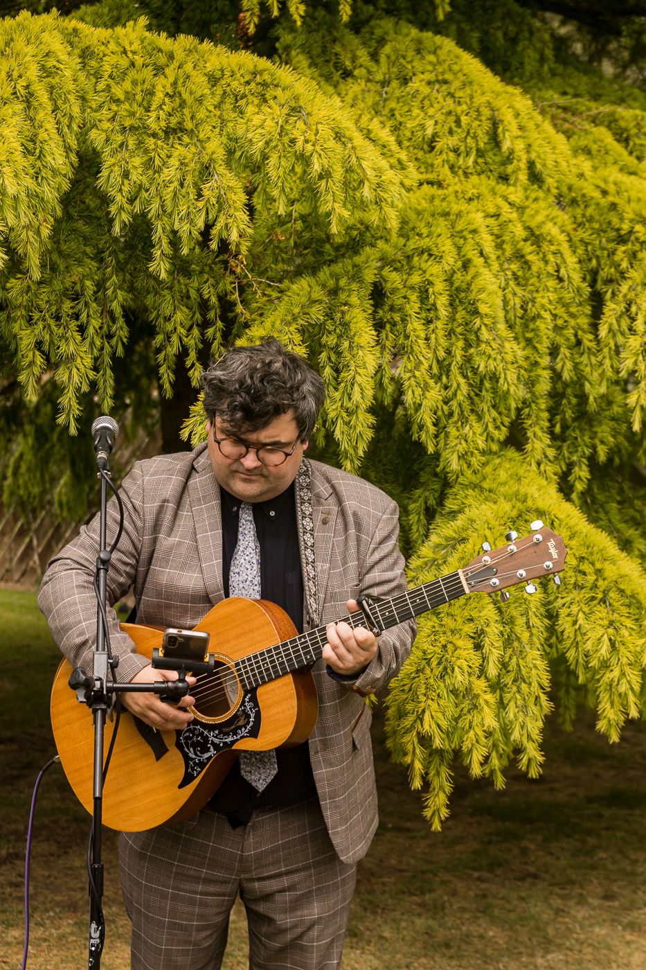 Musician plays acoustic guitar against backdrop of golden yellow foliage.