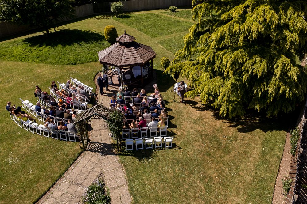 Aerial view of an outdoor wedding ceremony with guests seated in a curved arrangement.