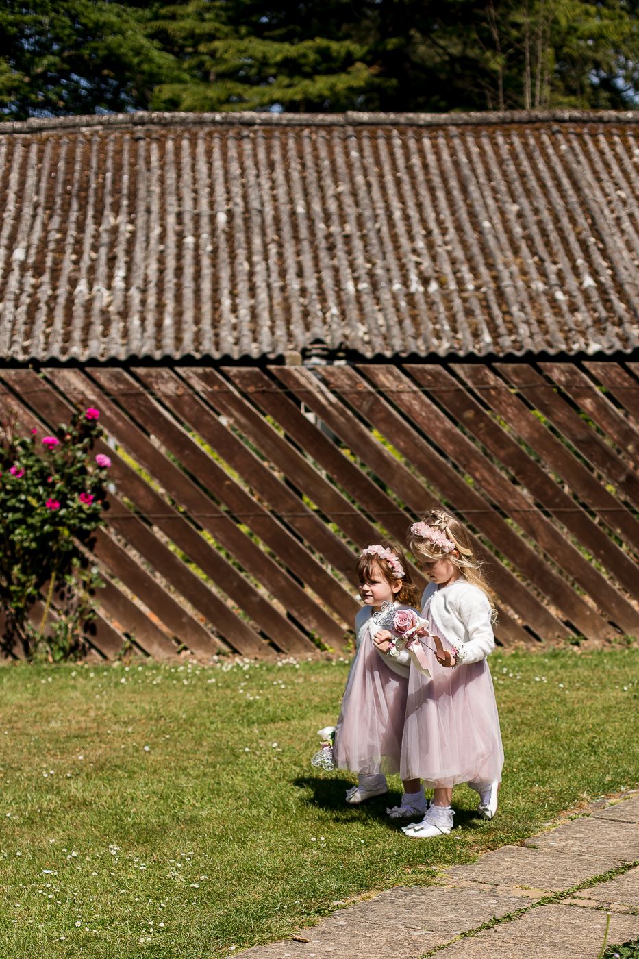 Two small attendants in light dresses walking along a garden path.