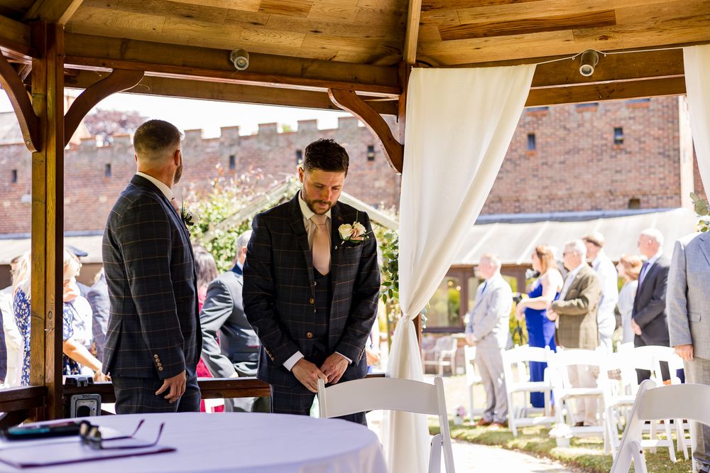 Wedding guests gather under an elegant wooden gazebo decorated with white fabric draping and floral arrangements.