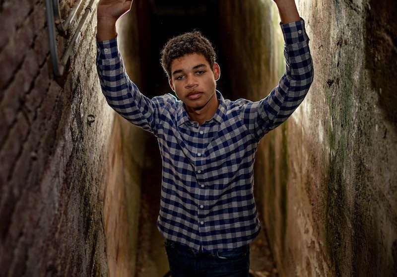 A person in a blue plaid shirt poses in front of a rustic wooden wall in a series of expressive shots.