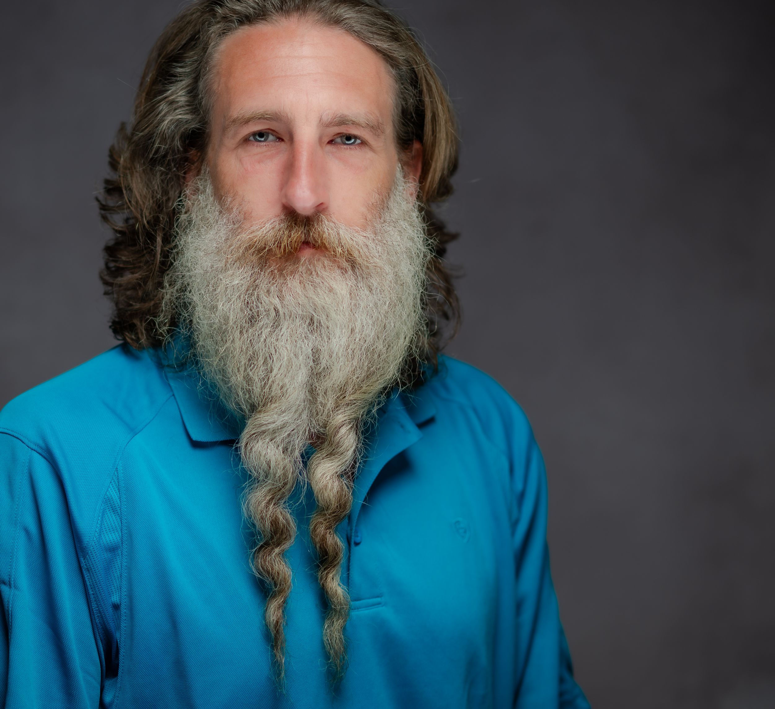 Portrait series showing a person with a long gray beard wearing a bright blue shirt against a dark background.
