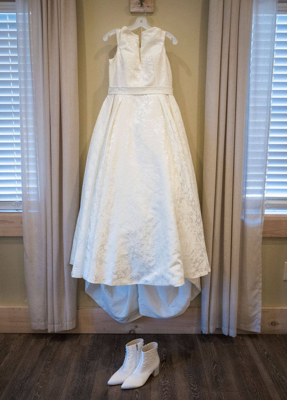 A white wedding dress and accessories displayed on hangers against a light colored curtained window.