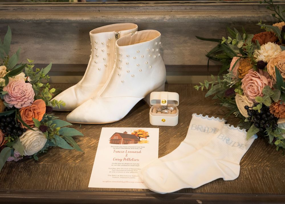 A vintage white Victorian-style lace-up boot displayed with delicate pink roses and greenery on a rustic wooden surface.