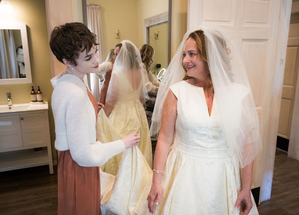 Wedding party members in formal attire gather for candid moments in a bright indoor hallway.