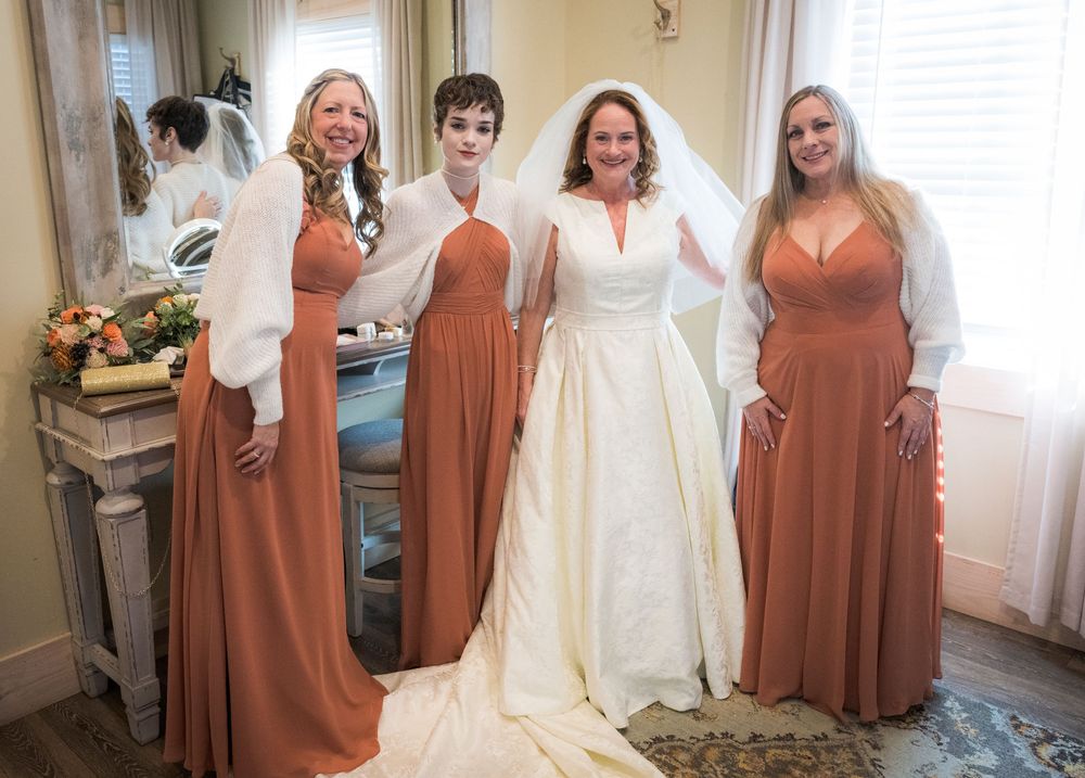Bridesmaids in rust-colored dresses gather around a bride in a white wedding gown.