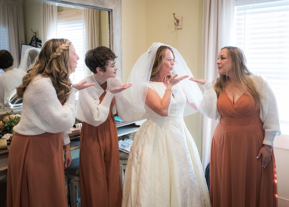 Wedding party members in terracotta dresses and white gowns pose together in a sunlit room.