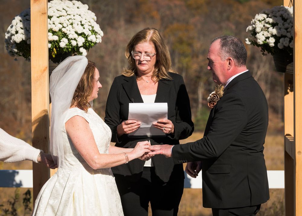 A sequence of wedding ceremony moments showing the exchange of rings and vows at a rustic venue with white floral decorations.