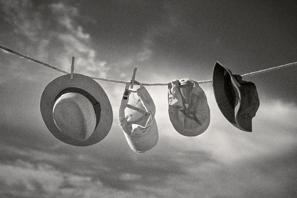 Black and white photograph of hats and shoes hanging to dry on a clothesline against a dramatic cloudy sky.