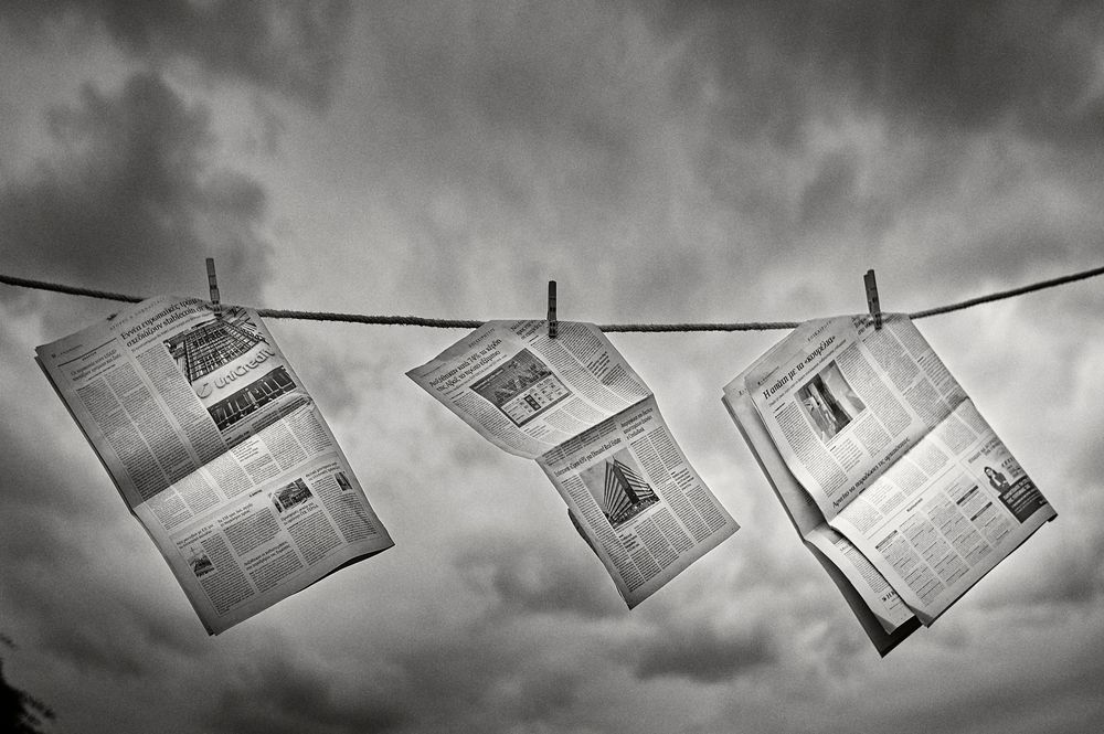 Dramatic black and white photograph of newspapers hanging from clotheslines against a cloudy sky.