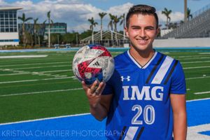 Athletes in blue and white uniforms pose with footballs on a sunny field with palm trees in the background.