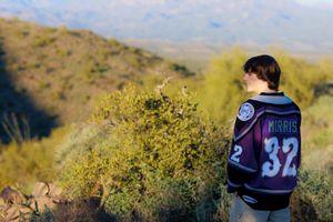 Person wearing a sports jersey stands on a hillside overlooking desert landscape with yellow flowering bushes.