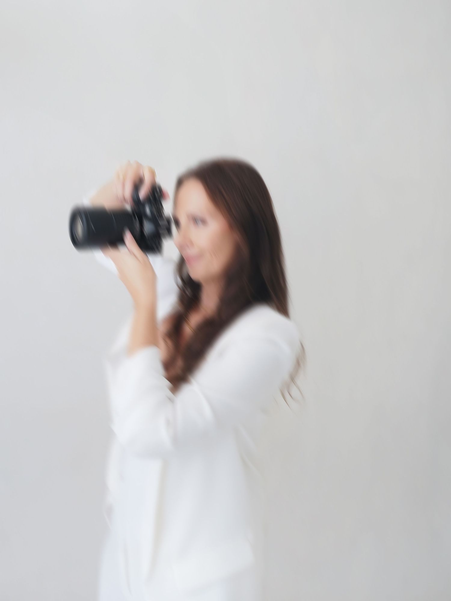Woman in white off-shoulder dress holding camera at beach setting.