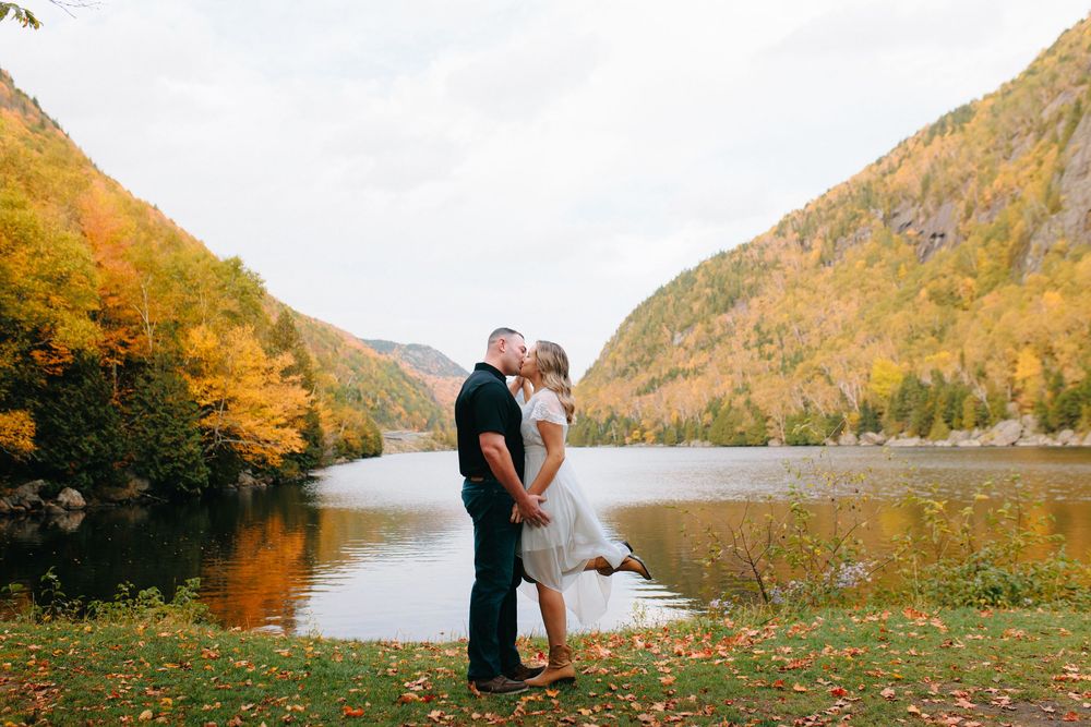 A scenic autumn wedding photo session by a lake surrounded by golden mountains and fall foliage.