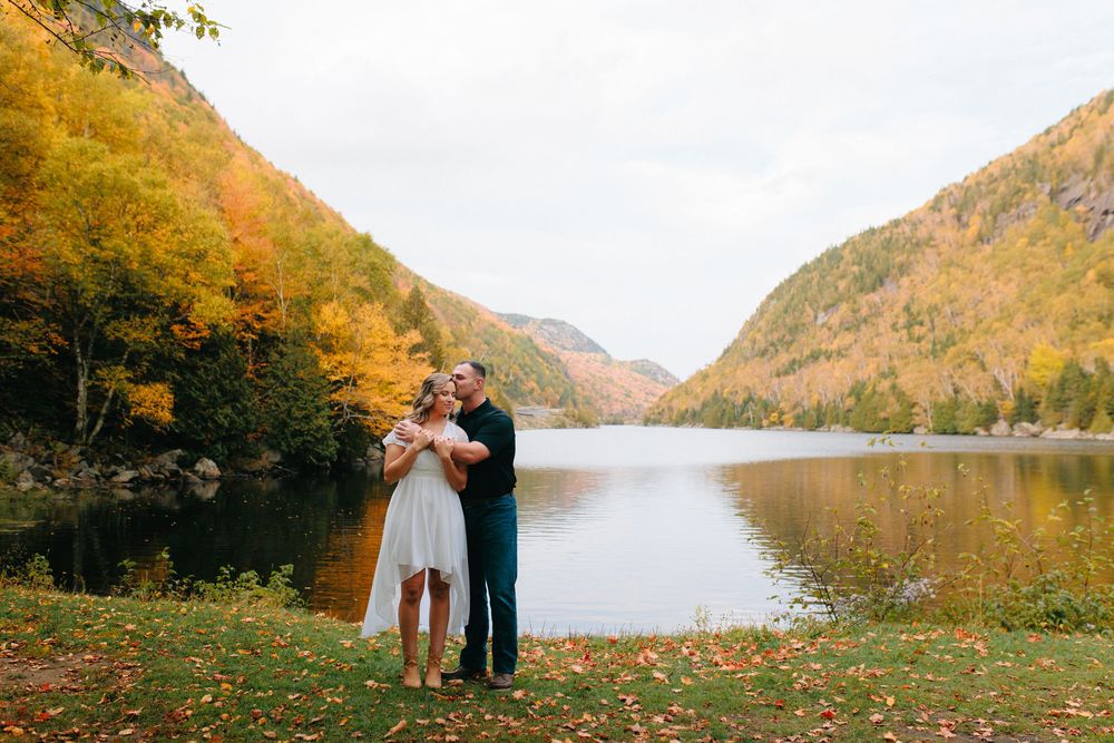 Panoramic autumn landscape of lake surrounded by mountains with golden foliage reflecting in calm waters.