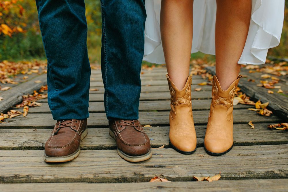 A row of feet wearing different styles of casual shoes and boots standing on a wooden deck with autumn leaves.