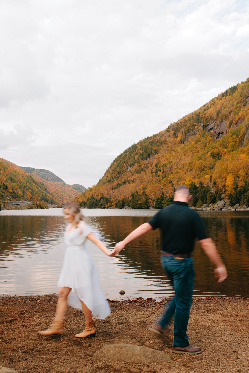 Couple dancing and spinning playfully by a scenic autumn lake with mountains in the background.