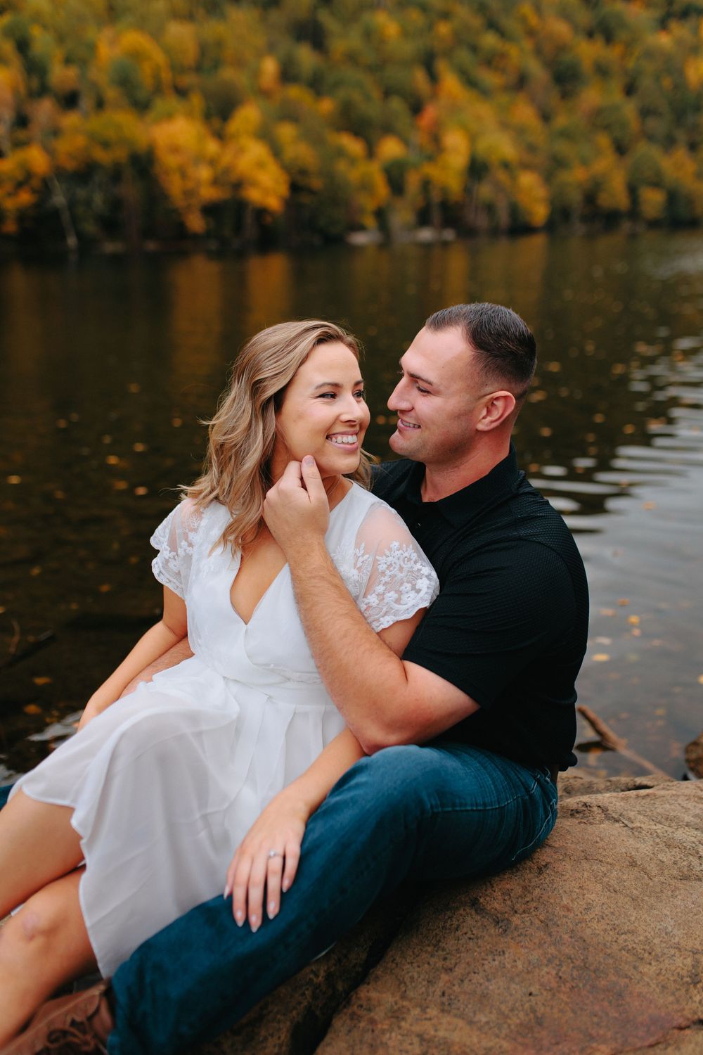 A couple shares a romantic moment while relaxing by a lake with autumn foliage reflecting in the water.