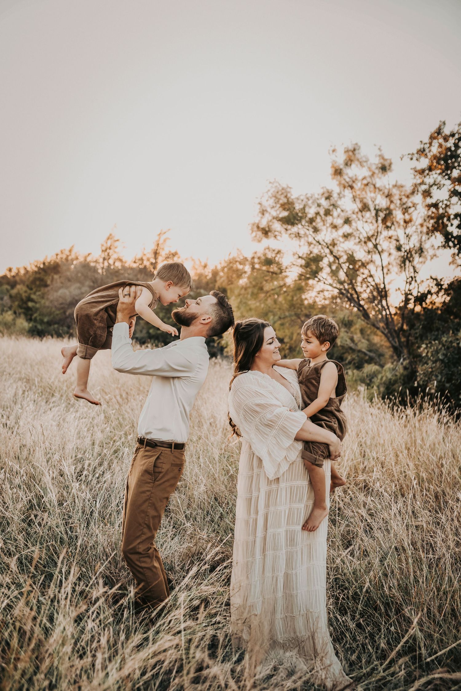 an excited flower mound family plays in a golden grass field at sunset as they celebrate baby number three