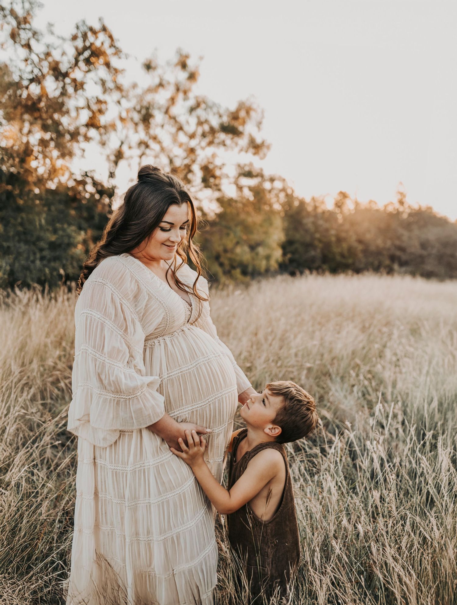 big brother snuggles his mom's belly at sunset in a field of golden grass for maternity photos