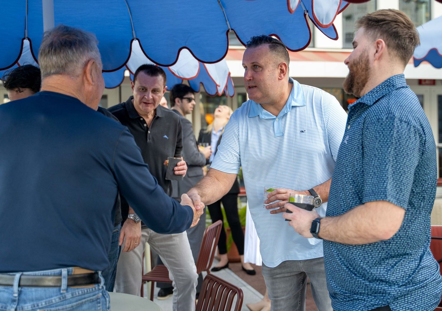 People gathered at an outdoor event under blue tents, socializing and networking in a casual setting.