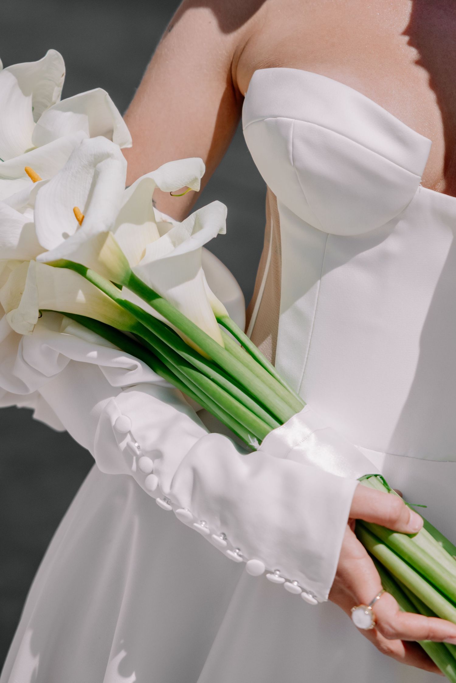 Close-up of white calla lily bouquet held against a white dress.