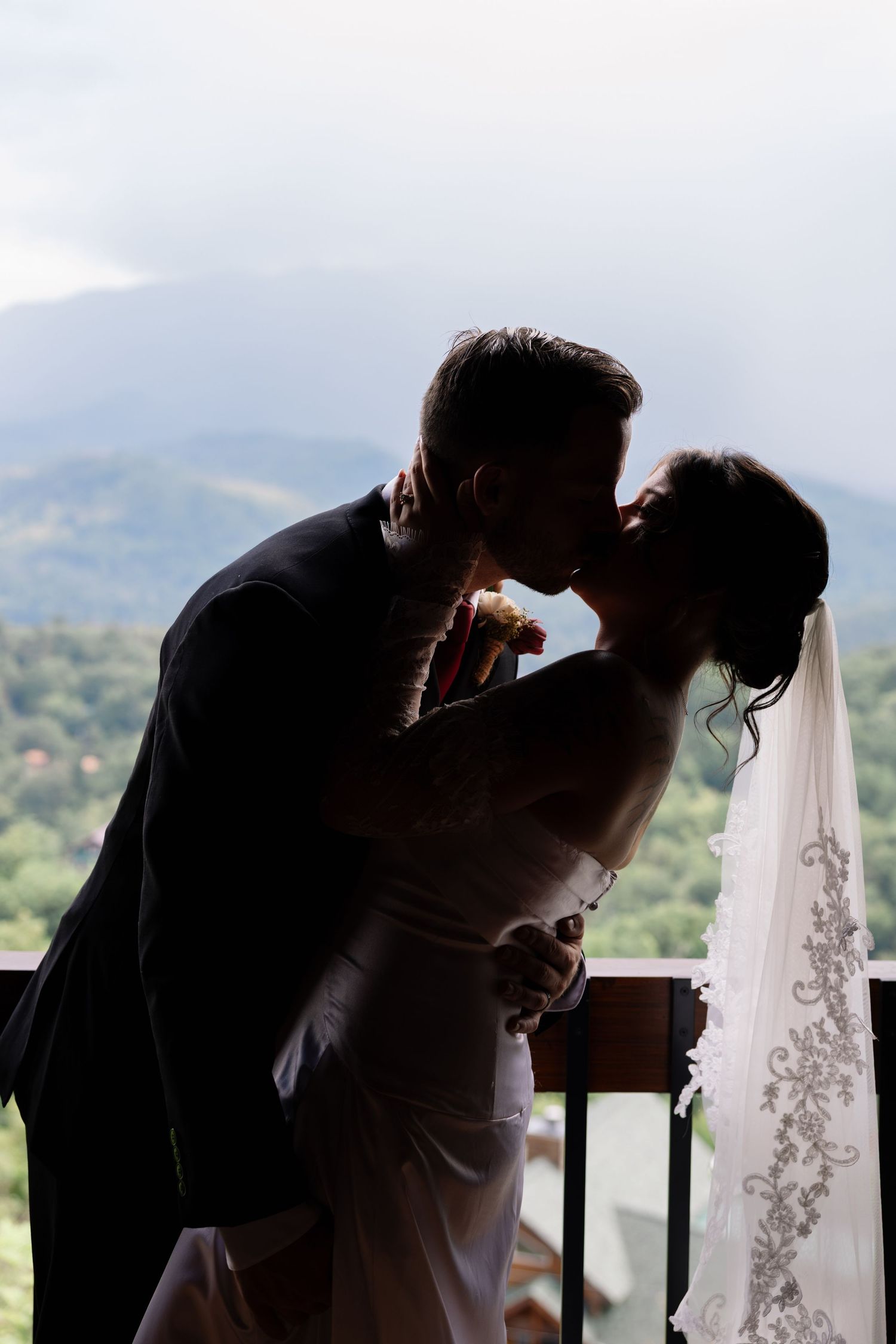 Silhouetted couple shares a romantic kiss on a balcony overlooking scenic mountain views in a series of wedding photos.