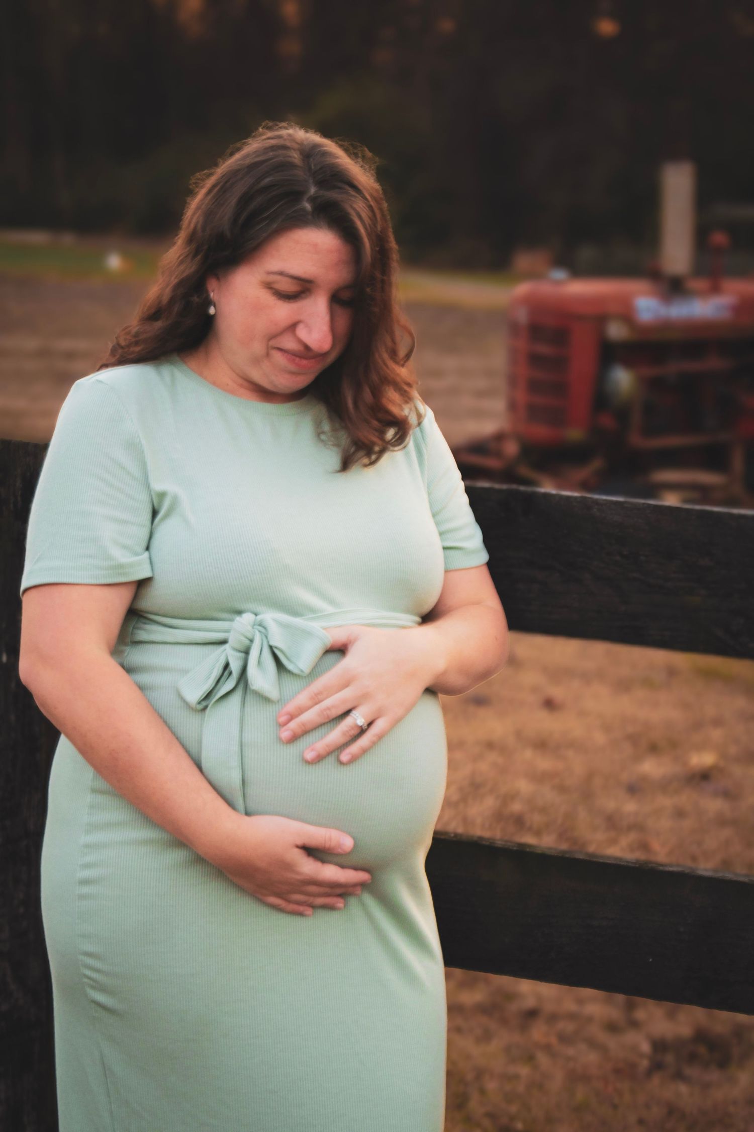 A woman in a mint green dress lovingly cradles her pregnant belly in an outdoor maternity photoshoot at sunset.