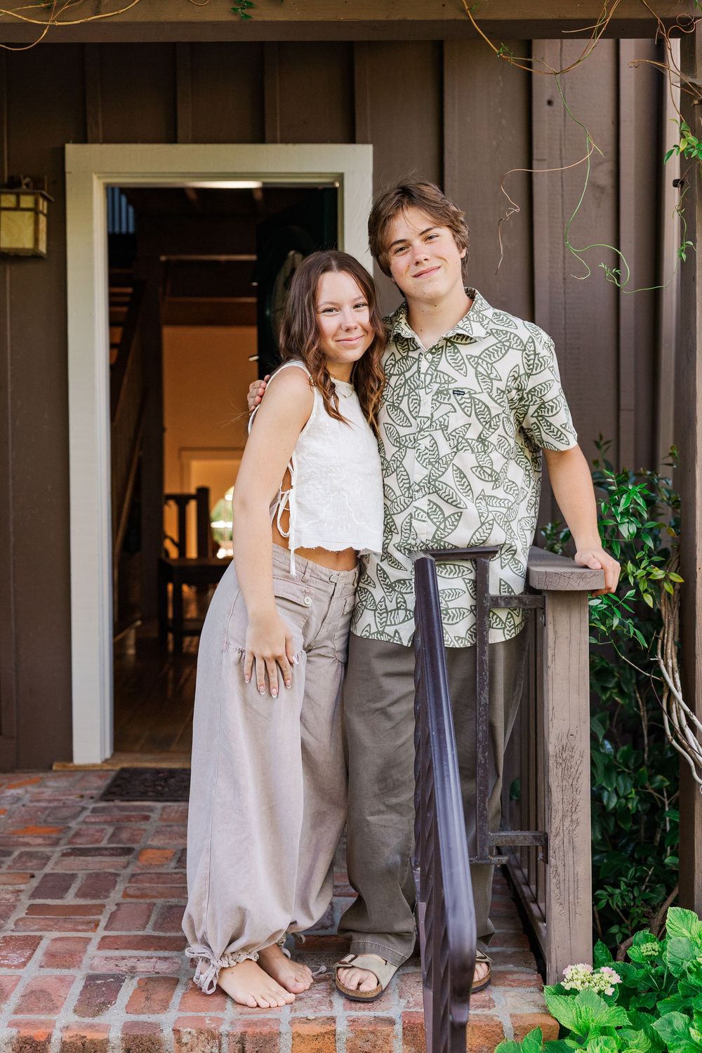A couple poses together under a wooden porch overhang with rustic brick flooring and climbing vines.