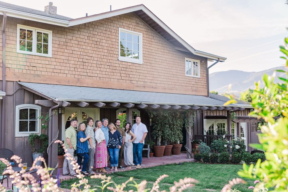 A panoramic view of a brick house exterior with a patio and green lawn during a sunny day.