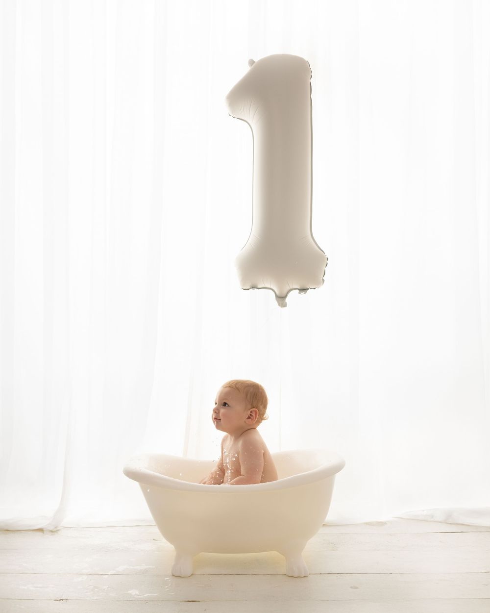Minimalist first birthday photoshoot with baby in vintage-style bathtub.