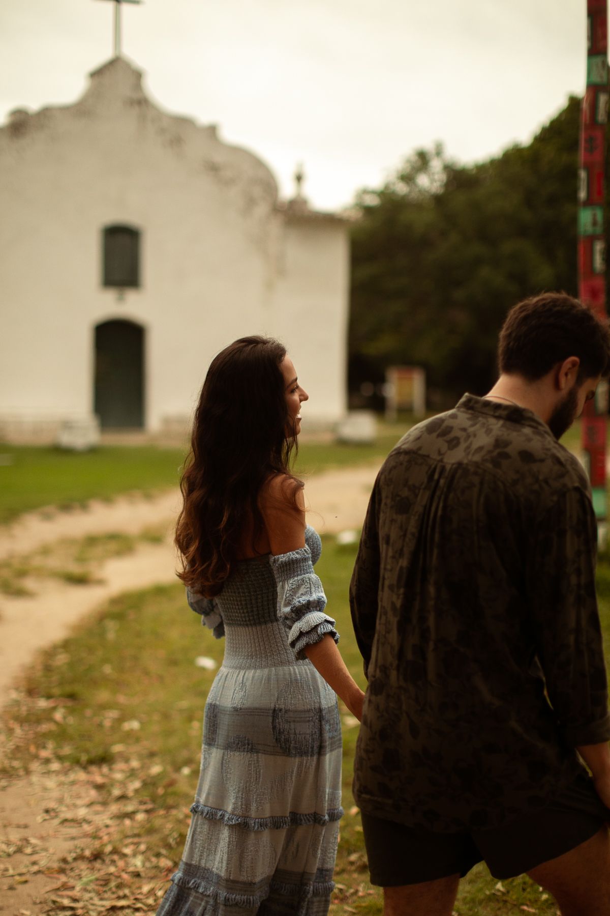 A couple walks together near a white church building on a cloudy day.