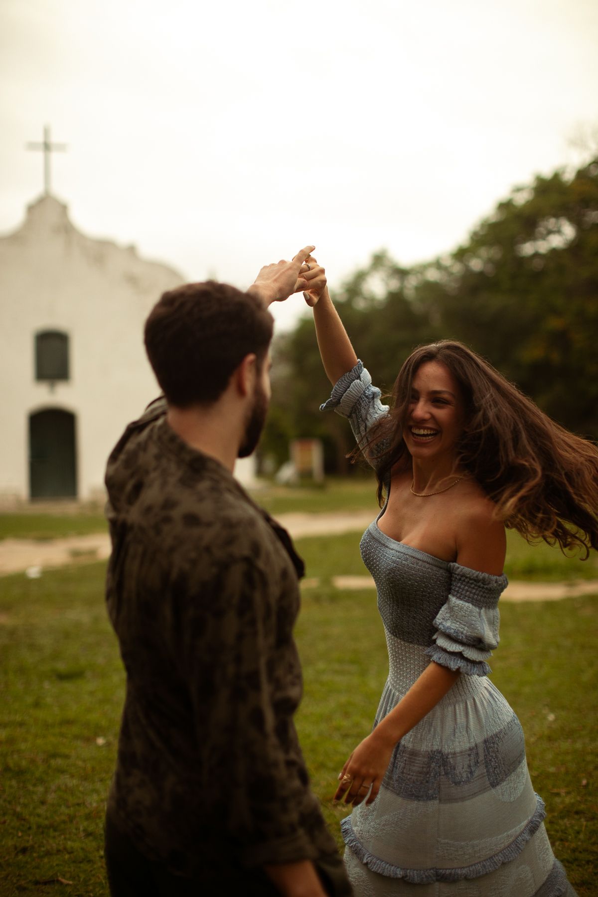 A couple dances joyfully together in front of a white church building during golden hour.