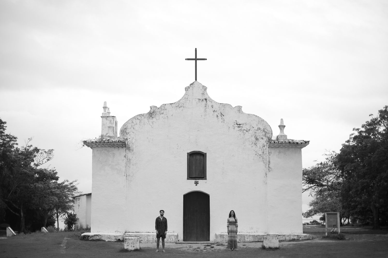 A row of white church buildings with crosses on top stand against a cloudy sky in a black and white photograph.