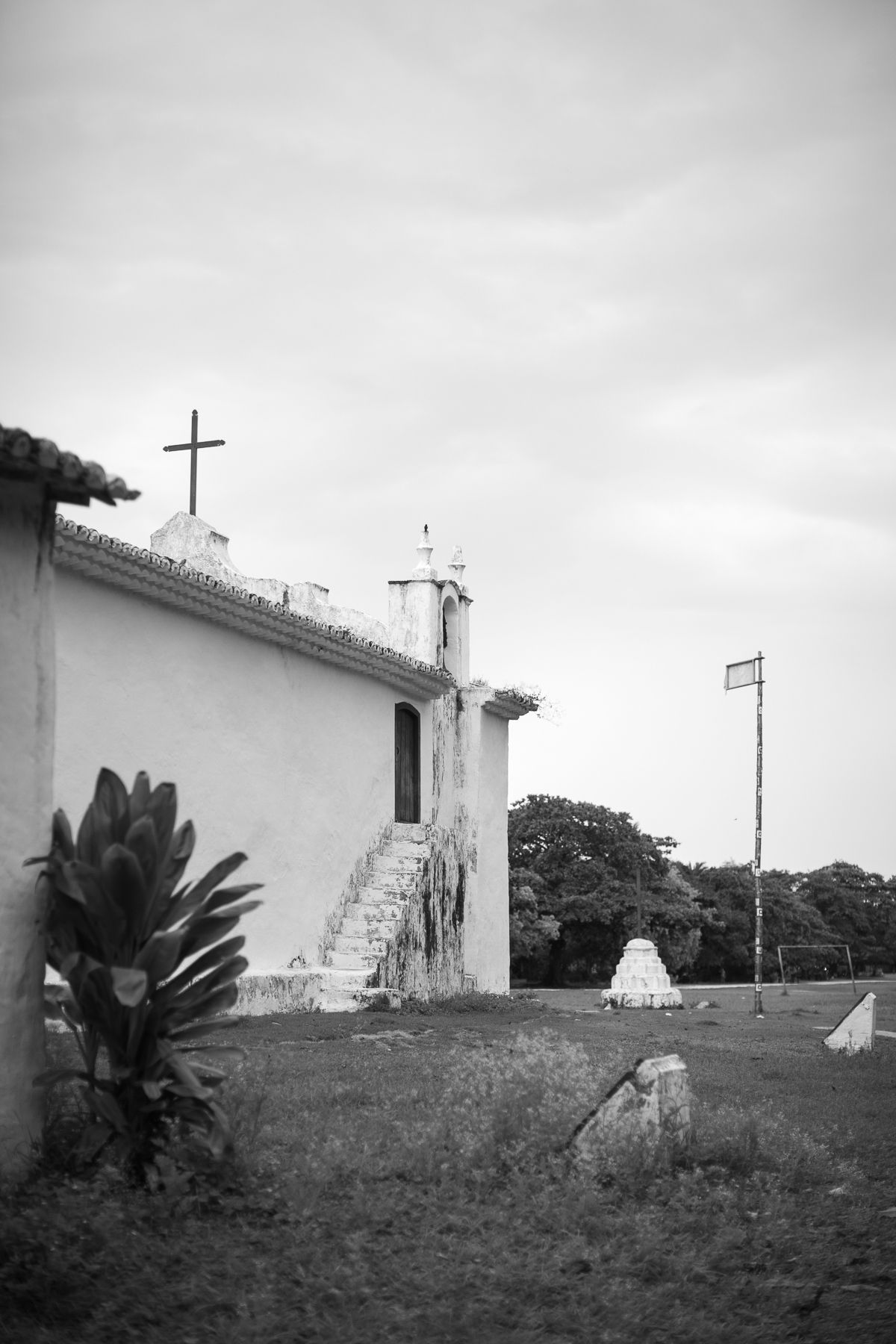 A white church with a cross on top stands against an overcast sky with palm trees in the foreground.