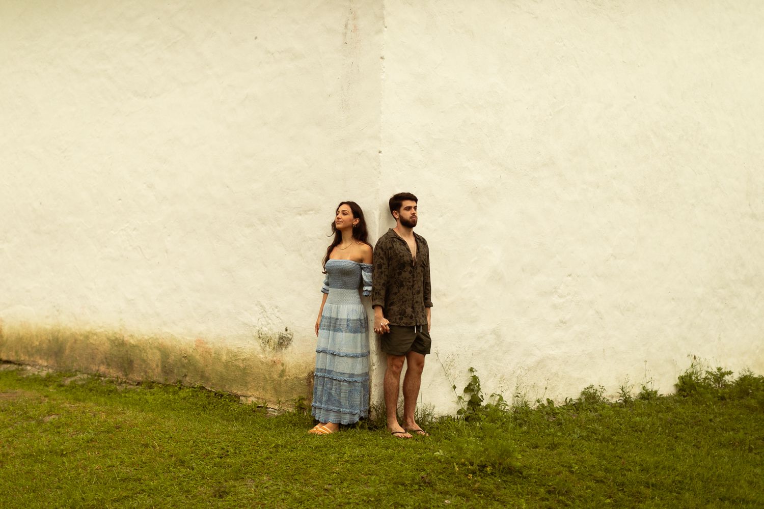 Two people sit together on a grassy hillside looking out at the view on a summer day.